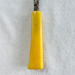 May include: A yellow plastic handle for a tool or knife. The handle is smooth and has a rounded shape.