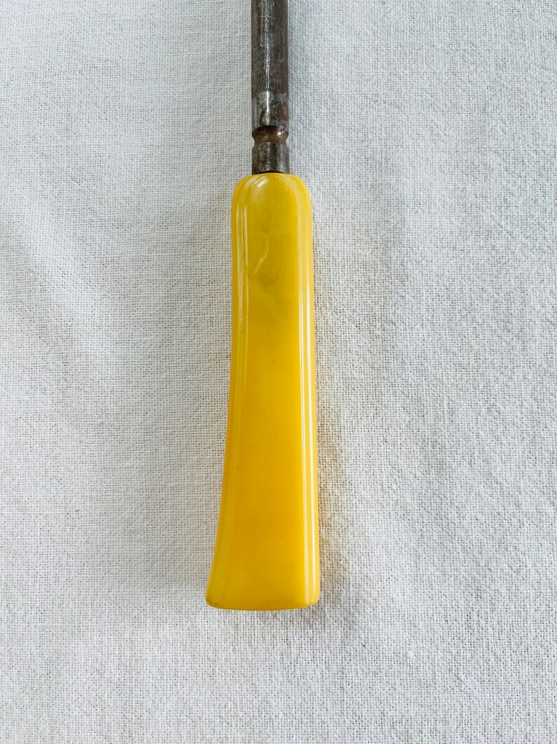 May include: A yellow plastic handle for a tool or knife. The handle is smooth and has a rounded shape.