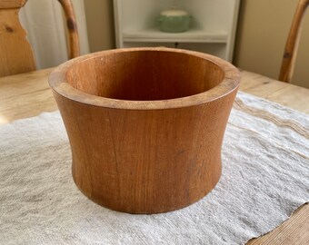 May include: A large, round, wooden bowl with a natural wood finish. The bowl is made of a light brown wood and has a smooth, rounded surface.