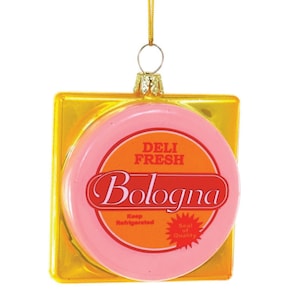 May include: A pink and gold Christmas ornament shaped like a package of bologna. The ornament has the text "Deli Fresh Bologna" and "Keep Refrigerated" on it.