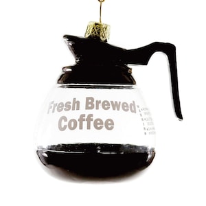 May include: A glass coffee pot ornament with a black handle and lid. The pot is filled with brown liquid and has the text "Fresh Brewed Coffee" printed on the side.