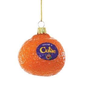 May include: A glass Christmas ornament shaped like a clementine with the text "You're a Cutie" on a purple label.