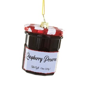 May include: A glass ornament shaped like a jar of raspberry preserve. The jar has a red and white lid and a white label that reads "Raspberry Preserve, Net Wt: 13oz (370g)".