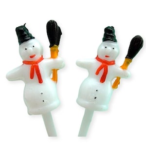 May include: Two white snowman cake toppers with black hats, red scarves, and black and orange brooms.