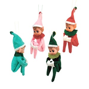 May include: Four vintage elf ornaments in various colors: teal, pink, green, and red. Each elf has a pointed hat, a ruffled collar, and white trim. The ornaments are suspended by thin white strings, perfect for holiday decorating.