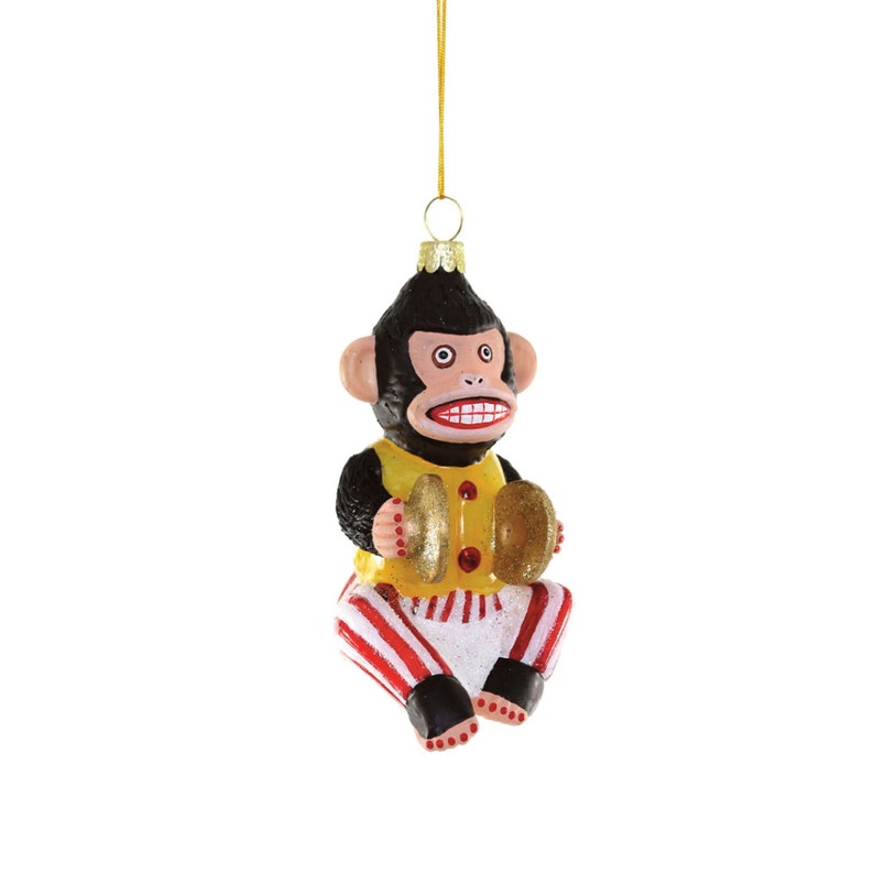 K&ouml;nnte beinhalten: Ein gl&auml;serner Weihnachtsbaumschmuck in Form eines Affen, der Becken spielt. Der Affe tr&auml;gt ein gelbes Hemd mit rot-wei&szlig; gestreiften Hosen. Der Schmuck hat eine goldene Schnur zum Aufh&auml;ngen.