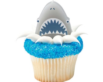 May include: A cupcake with blue sprinkles and white frosting topped with a gray shark fin cake topper.