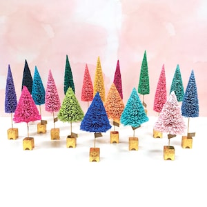 May include: A collection of twenty miniature bottle brush trees in various vibrant colors including pink, blue, green, yellow, and purple. Each tree is mounted on a small, square, gold-colored base and features a thin, metallic stem.