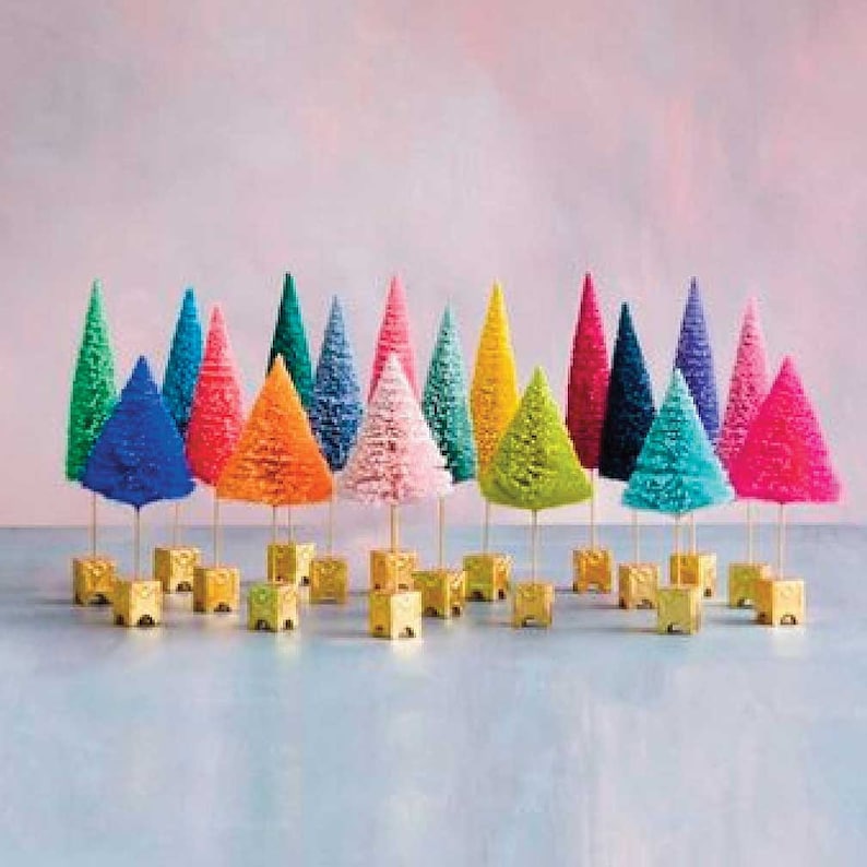 May include: A collection of twenty miniature bottle brush trees in a vibrant array of colors including pink, blue, green, orange, yellow, and purple. Each tree is mounted on a thin wooden stem attached to a small, square, gold-colored base.