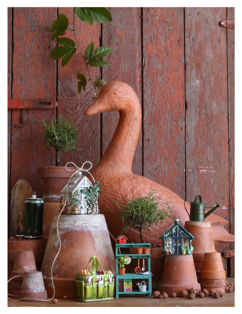 Pode incluir: Uma est&aacute;tua de pato de terracota &eacute; o ponto focal desta exibi&ccedil;&atilde;o com tema de jardim. Estufas em miniatura, um banco de vasos e um regador verde s&atilde;o dispostos com plantas em vasos e vasos de terracota contra um fundo de madeira vermelha.