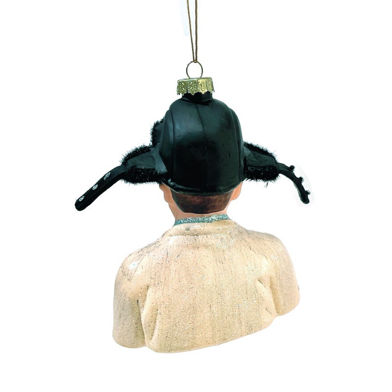 May include: A Christmas ornament depicting a person wearing a black hat with ear flaps. The ornament is a bust, showing the back of the person's head and shoulders. The hat has a fur trim and the person is wearing a light-colored jacket.