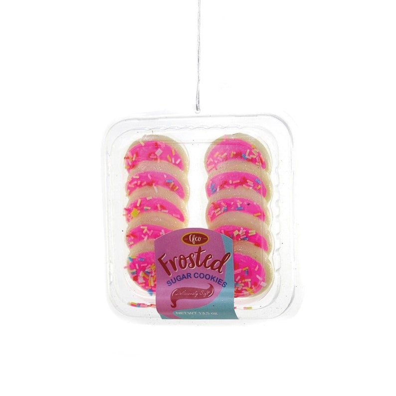 May include: A clear plastic container holding frosted sugar cookies. The cookies are round with pink frosting and colorful sprinkles. The label reads "Frosted Sugar Cookies" in pink and red.
