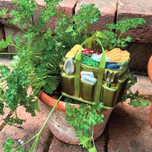 Pode incluir: Um enfeite decorativo com tema de jardim em um vaso de terracota com salsa. O enfeite &eacute; uma sacola dourada cheia de vegetais em miniatura, ferramentas de jardinagem e as palavras "Rabanete" e "Cenoura" em etiquetas.