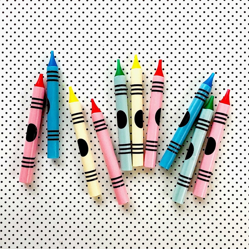 May include: A collection of ten crayons in various colors, including blue, green, red, yellow, and black. The crayons are arranged in a fan shape on a white background with black polka dots.