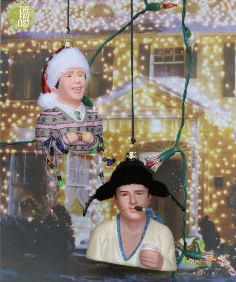 May include: Two Christmas ornaments depicting characters from a holiday movie. One ornament features a figure wearing a Santa hat and a sweater, while the other has a fur hat and a cigar. The background is a blurred image of a house with Christmas lights.
