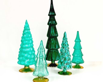 May include: A collection of six decorative glass Christmas trees in varying shades of green and teal. Each tree has a textured surface and sits on a gold-colored base. The trees range in size and shape, creating a festive display.
