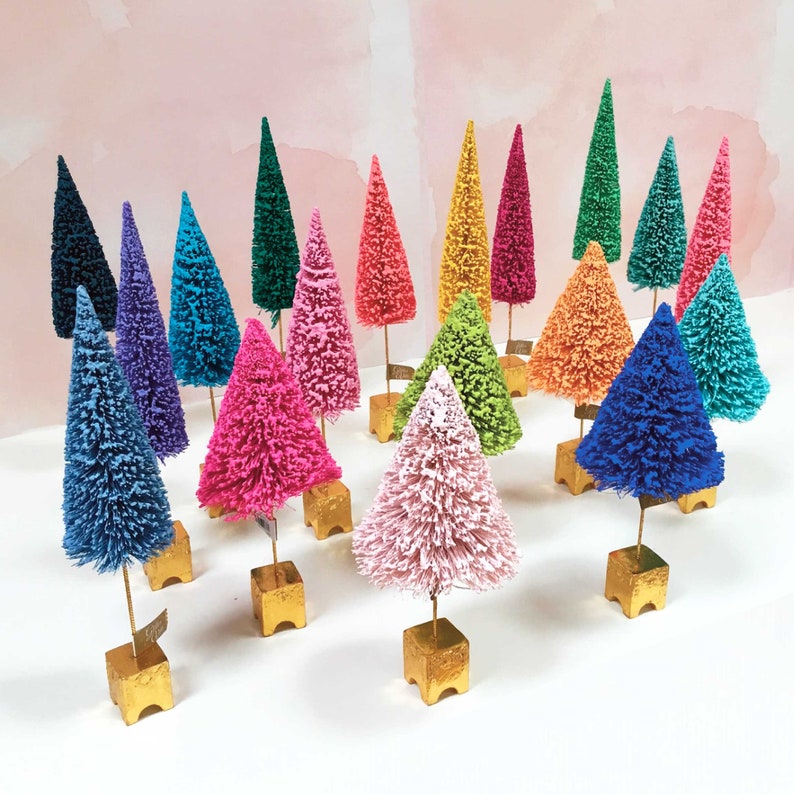 May include: A collection of miniature bottle brush trees in a variety of vibrant colors including pink, blue, green, yellow, orange, and purple. Each tree is mounted on a small, square, gold-colored base, creating a colorful display of decor.