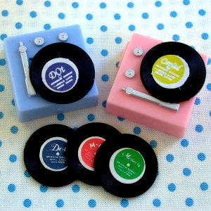 May include: Three miniature record players with black vinyl records and colorful labels. The labels read "Dot", "Mercury", and "Capita".