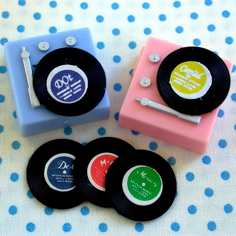 May include: Three miniature record players with black vinyl records and colorful labels. The labels read "Dot", "Mercury", and "Capita".