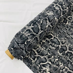 Peut inclure: Un rouleau de tissu imprimé serpent noir et blanc. Le tissu a une surface texturée et est parfait pour les projets de bricolage.