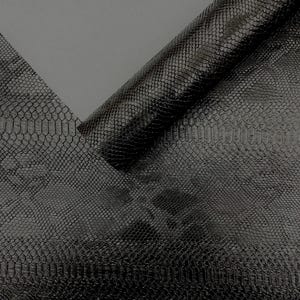 May include: Black faux leather material with a snakeskin pattern. The material is partially rolled up, revealing the underside. The texture is glossy and the color is a deep black.
