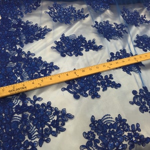 Puede incluir: Tela de encaje floral azul real con lentejuelas sobre un fondo de malla transparente. Se incluye una regla para la escala.
