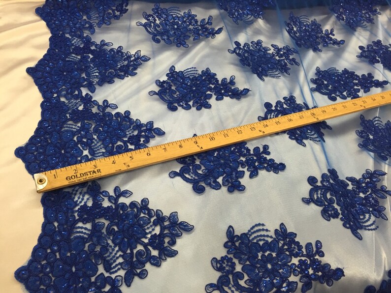 Puede incluir: Tela de encaje floral azul real con lentejuelas sobre un fondo de malla transparente. Se incluye una regla para la escala.