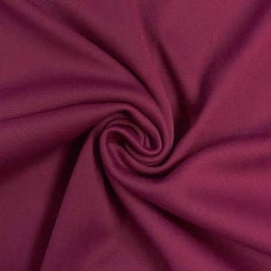 Könnte beinhalten: Ein einfarbiger, tief magentafarbener Stoff mit einer glatten, matten Textur. Das Material ist in einer zentralen Spirale angeordnet, wodurch weiche, fließende Falten und Schatten entstehen, die die gleichmäßige, satte Farbe betonen.