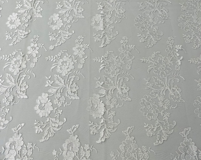 White floral design embroider and corded on a mesh lace fabric-sold by the yard.