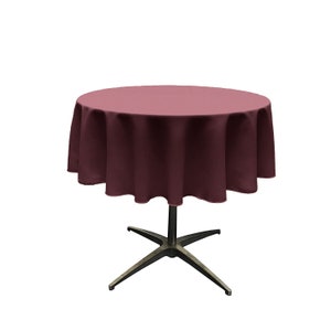 May include: A round burgundy tablecloth draped over a dark metal table base. The tablecloth is a solid color and covers the entire table surface. The table base has a star-shaped design.