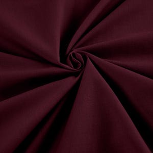 May include: A close-up of a deep burgundy fabric, tightly swirled to create a spiral effect. The fabric's texture is visible, with subtle variations in the rich, dark red colour. The folds and shadows add depth to the image.