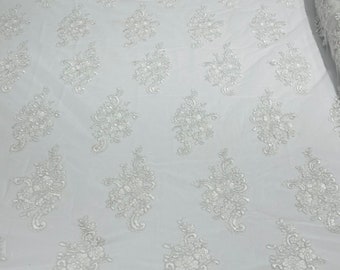 White floral design embroidery on a mesh lace with sequins and cord-sold by the yard.