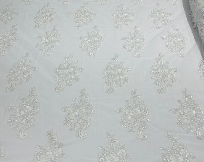 White floral design embroidery on a mesh lace with sequins and cord-sold by the yard.