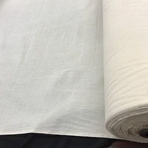 May include: A roll of white cotton fabric, unbleached and natural, with a smooth texture. The fabric is rolled up and ready to be used for sewing, quilting, or other crafts.