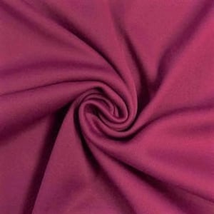 Könnte beinhalten: Ein einfarbiger magentafarbener Stoff mit einer glatten, matten Textur. Das Material ist in einer zentralen Spirale gerafft, wodurch weiche, fließende Falten und tiefe Schatten entstehen, die die gleichmäßige, kräftige Farbe betonen.