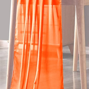 May include: Orange table runner made of sheer fabric. The runner is draped over a wooden table.