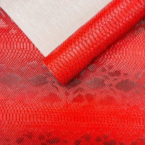 Puede incluir: Primer plano de un rollo y una lámina plana de cuero rojo vibrante con estampado de piel de serpiente. El material tiene un patrón escamoso texturizado, con variaciones en el tono rojo. El cuero se utiliza probablemente para artesanía o moda.