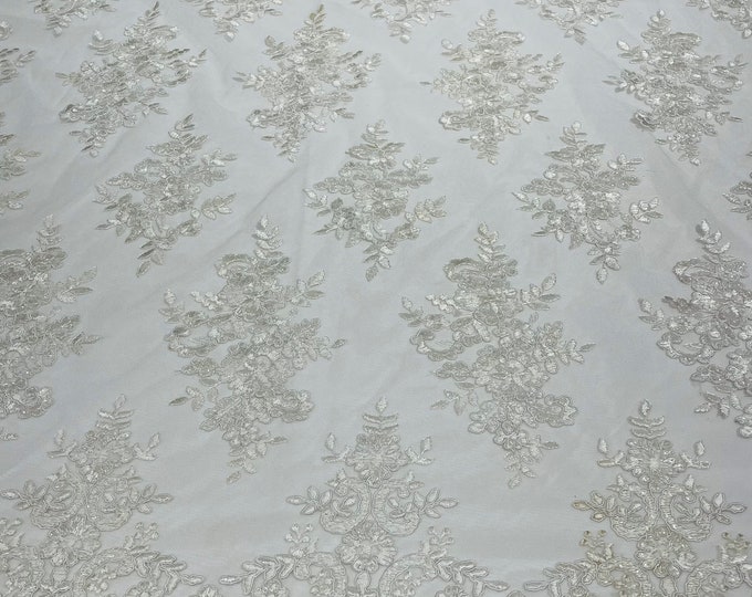 White corded flowers embroider with sequins on a mesh lace fabric-sold by the yard.