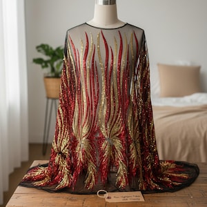 Puede incluir: Una tela negra transparente con un intrincado patrón de llamas bordado con lentejuelas rojas y doradas brillantes. La tela está colocada sobre un maniquí, mostrando un diseño vertical repetitivo que irradia desde el dobladillo inferior.