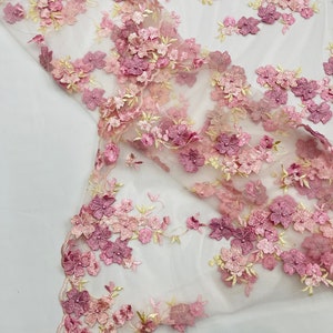 Könnte beinhalten: Zarter Spitzenstoff mit floralen Stickereien in Rosa- und Mauve-Tönen, mit Akzenten in blassem Gelb. Die dreidimensionalen Blumen erzeugen einen strukturierten Effekt. Ideal für Brautmode oder Dekorationsprojekte.