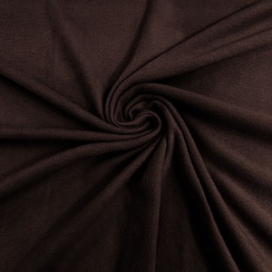May include: A close-up of a brown fabric with a soft, fuzzy texture. The fabric is folded and draped, creating a swirling pattern.