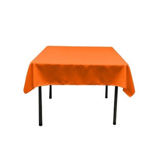 May include: Orange square tablecloth with black metal legs. The tablecloth is made of a smooth, wrinkle-resistant fabric.