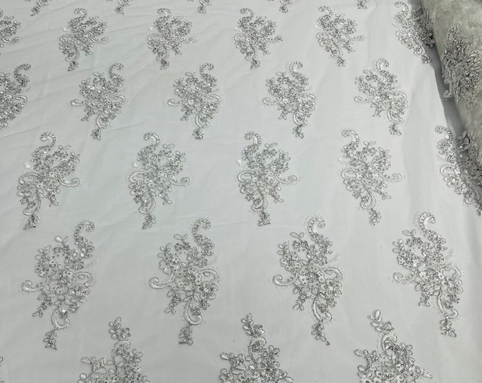 White Silver floral design embroidery on a mesh lace with sequins and metallic cord-sold by the yard.