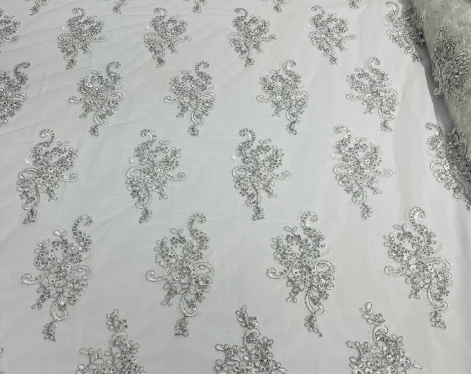 White Silver floral design embroidery on a mesh lace with sequins and metallic cord-sold by the yard.