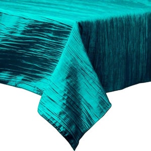 Puede incluir: Un mantel de mesa azul turquesa con textura arrugada. El mantel está hecho de un material suave y sedoso y tiene un brillo sutil.
