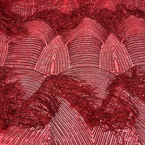 Könnte beinhalten: Roter Paillettenstoff mit geometrischem Muster und Fransen-Details. Der Stoff hat eine durchsichtige Mesh-Rückseite.