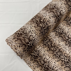 Op de afbeelding: Een rol bruine en beige stof met een slangenhuidpatroon.