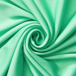 Könnte beinhalten: Ein einfarbiger, mintgrüner Stoff mit glatter Textur, der in einem engen, wirbelnden Spiralmuster angeordnet ist, wodurch tiefe, fließende Falten und Schatten entstehen, die vom Zentrum ausgehen und die gleichmäßige Farbe betonen.