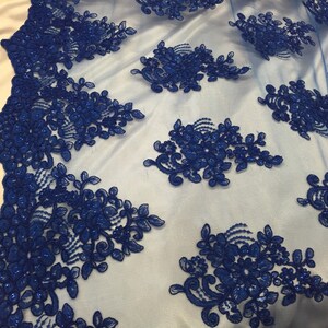 Puede incluir: Tela de encaje floral azul real con un delicado patr&oacute;n de flores y hojas. El encaje est&aacute; adornado con cuentas y tiene un respaldo de malla transparente.