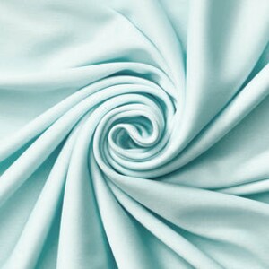 Könnte beinhalten: Ein einfarbiger, heller mintgrüner Stoff mit einer glatten, matten Textur. Das Material ist in einer engen, zentralen Spirale angeordnet, wodurch tiefe, strahlenförmige Falten und Schatten entstehen, die die weiche Farbe und den Fall betonen.